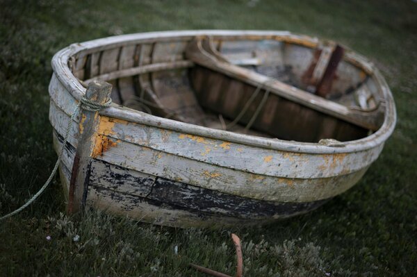 An old faded boat is standing on the green grass