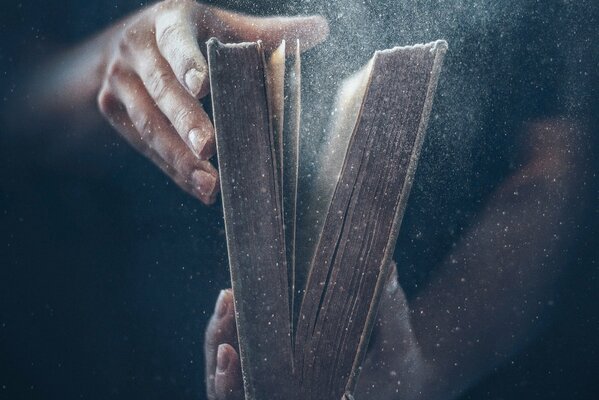 Die Hände halten ein altes Buch, aus dem Staub fliegt