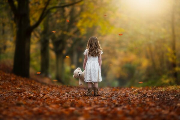 Una niña con un oso de peluche en las hojas de otoño