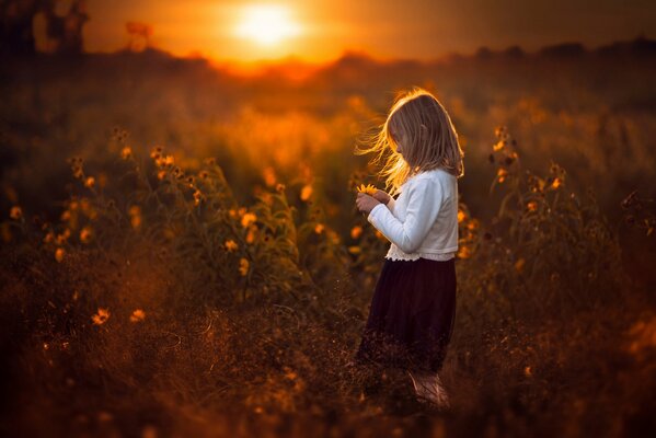 Niña con una flor en sus manos en el fondo de la puesta de sol