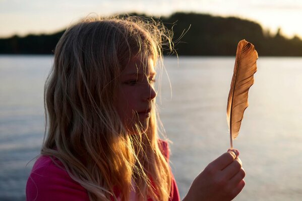 A girl in the sunlight looks at a feather