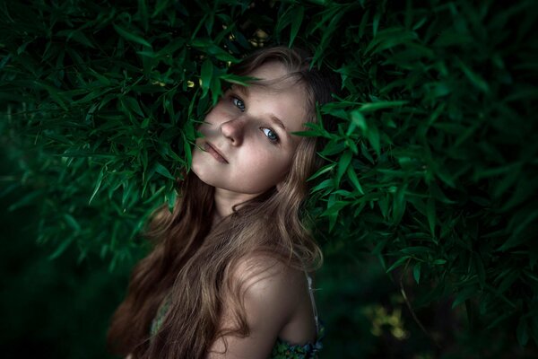 A long-haired girl with freckles in the middle of greenery