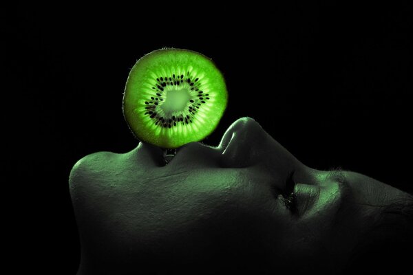 Un hombre sostiene con sus labios una rodaja de kiwi iluminada por una linterna