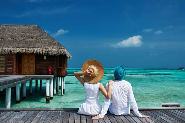 Couple en blanc assis sur une passerelle vers un bungalow dans la mer