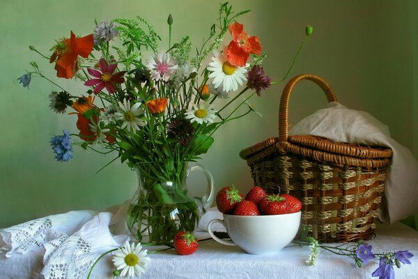 A jug, strawberries and a basket stand on a table against the wall