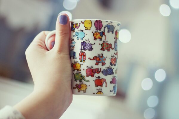 The girl holds a mug with elephants in her left hand