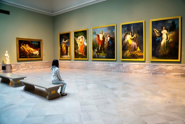 A girl is sitting in a museum and looking at paintings