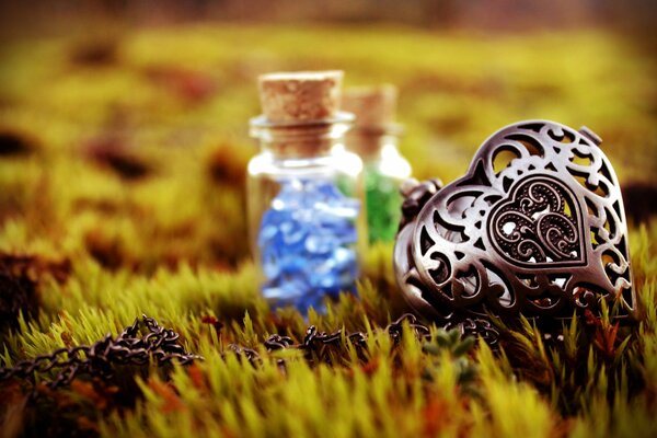 A forged heart pendant on a chain and small bottles with magical contents. photo on the grass