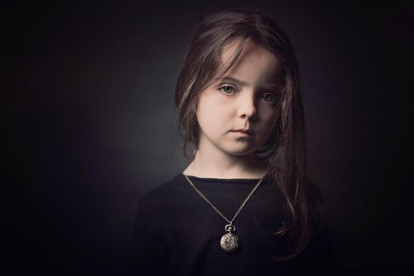 Retrato de una niña en negro con un gran colgante