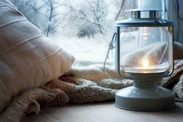 Kerosinlampe, Plaid und Kissen auf der Fensterbank vor dem Hintergrund des Winters vor dem Fenster