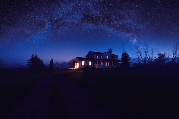 Casa con ventanas iluminadas y cielo estrellado nocturno