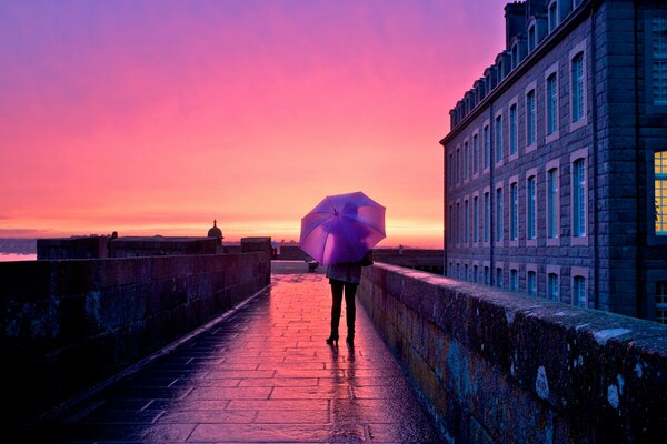 A girl under an umbrella in the middle of the city at sunset