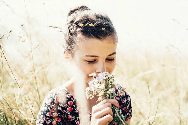 A girl in the summer in the field sniffs a bouquet