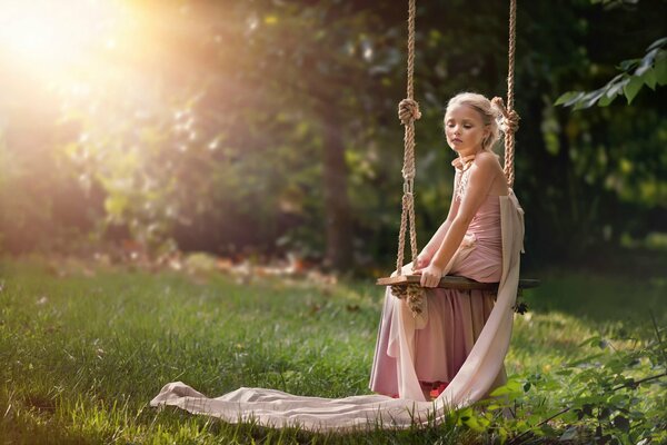 Mädchen im Kleid sitzt ruhig auf einer Schaukel in der Sonne im Sommer Tapete