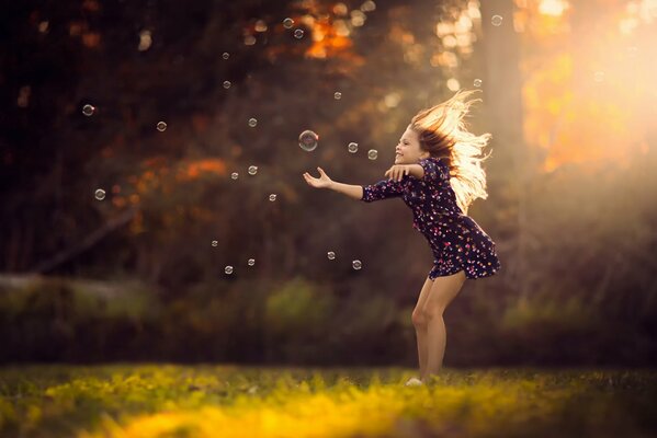 A girl in a dress catches soap bubbles