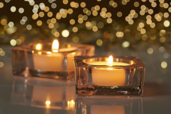 Burning candles in beautiful square glass candlesticks. small lights. blurred background