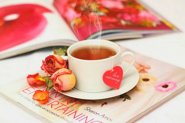 A cup of tea on a magazine surrounded by rose petals