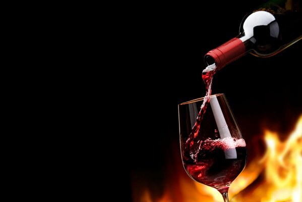 Con una botella de vino tinto se vierte el vino en un vaso detrás de la llama