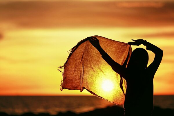 A sweet and peaceful girl on the background of a sunset with a scarf