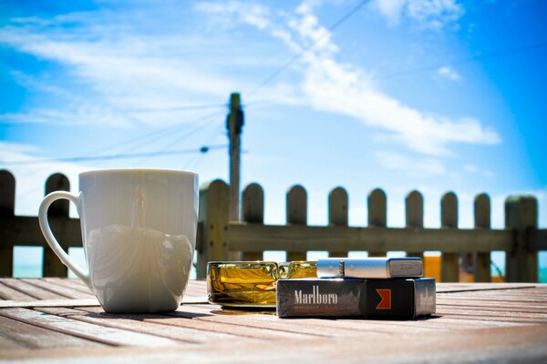 Tasse, Aschenbecher, Feuerzeug und Zigaretten auf einem blauen Himmelshintergrund