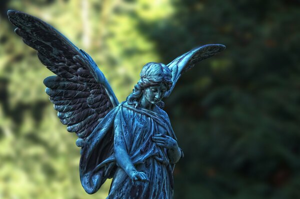 Estatua de ángel con alas en el fondo de los árboles