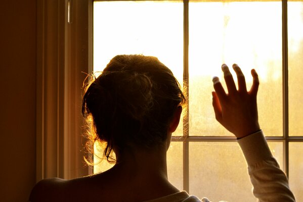 The girl, with her hand raised, looks out the window