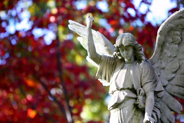 Sullo sfondo di alberi verdi e rossi scultura di un angelo con le ali