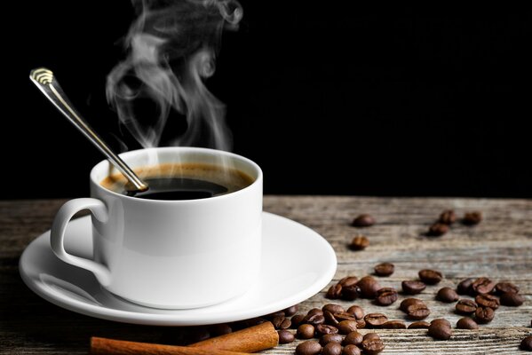 A mug of hot aromatic coffee stands on a table on which coffee beans and cinnamon are scattered