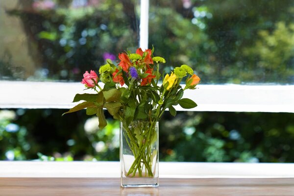 A bouquet of flowers on the windowsill against the background of a window with greenery