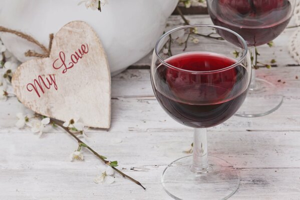 Ein Glas Rotwein mit einem hölzernen Herz auf einer Holzoberfläche