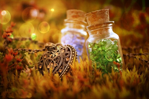 Among the grass are bottles with different stones and a heart-shaped pendant