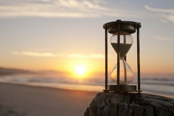 Reloj de arena en el fondo de la playa con el mar en el fondo de la puesta de sol fondo de pantalla
