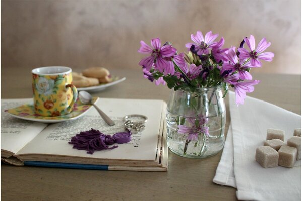Filiżanka ze spodkiem, ciasteczka i kostki cukru. delikatne różowe kwiaty w przezroczystym wazonie. ujawniona książka