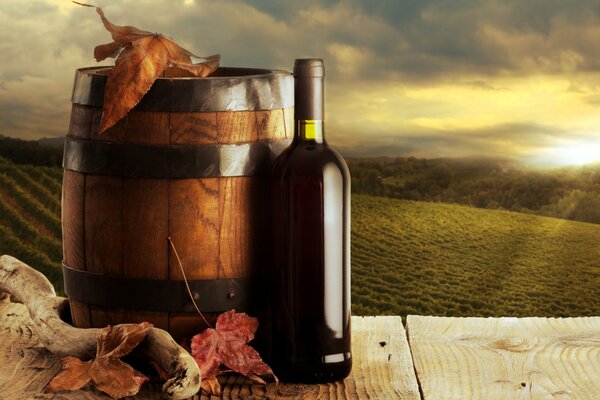 Una botella oscura de vino junto a un barril de roble contra el telón de fondo de largos viñedos en la puesta del sol de otoño