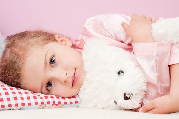 Photo d une jeune fille se trouve sur un oreiller dans une étreinte avec un ours en peluche