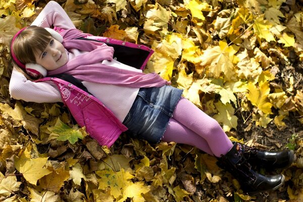 A girl in pink clothes is resting on yellow leaves