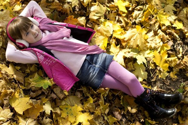 Девочка в розовой одежде отдыхает на жёлтых листьях