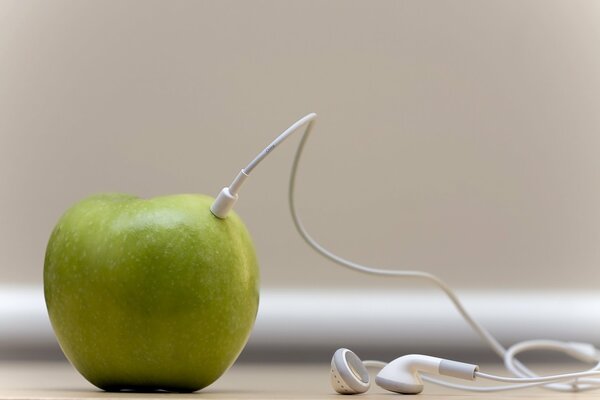 White headphones are connected to a green apple