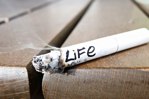 Дымящаяся недокуренная сигарета со словом жизнь написанным по-английски