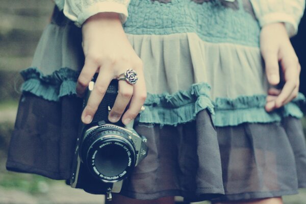 Mädchen in einem blauen Kleid mit einer Kamera in den Händen und einem Ring am Finger