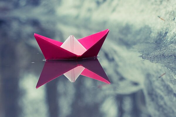 Pływająca papierowa, różowa łódka w odblaskowej zimowej wodzie