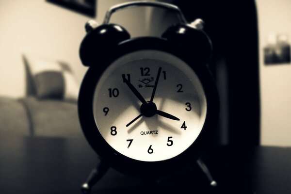 In the black-and-white photo, there is an alarm clock on the table.