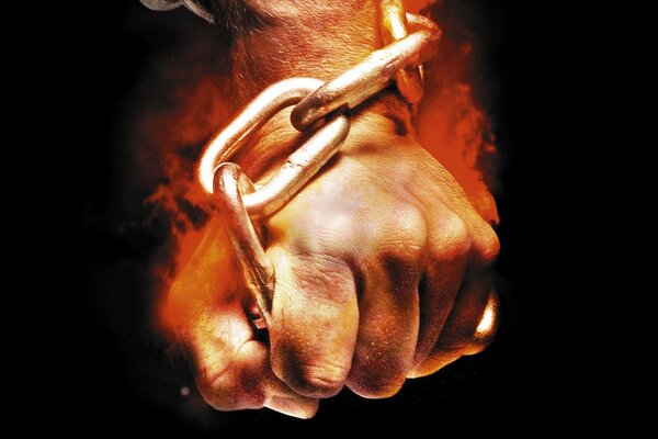 On a black background, a fist on fire holds a chain