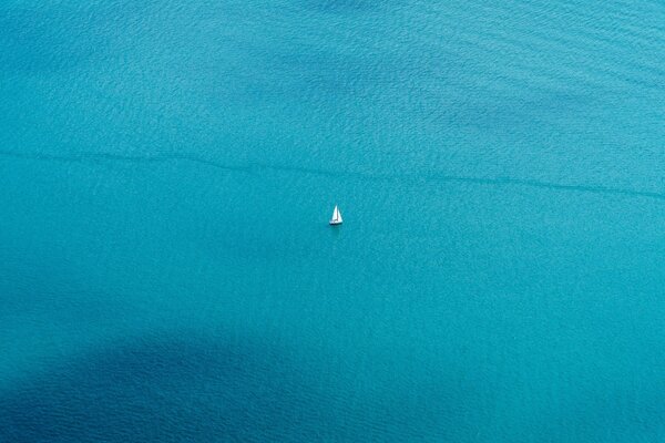 Lejos de la costa, en el mar azul, un barco navega y solo se ve una vela blanca