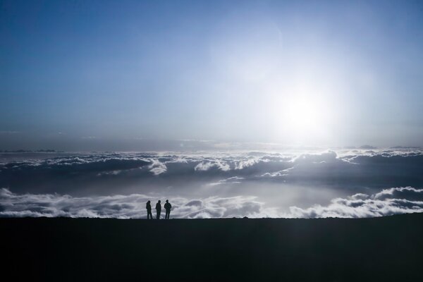 Menschen auf einem Berg auf Augenhöhe mit den Wolken unter den Sonnenstrahlen