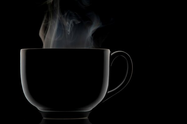 Tazza nera da cui il vapore va su sfondo nero