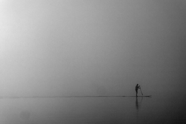 Mężczyzna we mgle robiący paddleboarding na morzu