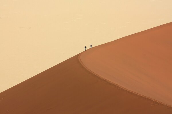 Zwei Menschen klettern in der Wüste auf eine Düne