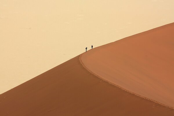 Two people climb a dune in the desert