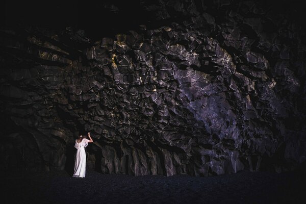 Una chica con un vestido blanco se apoya en una roca